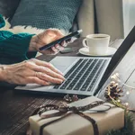 Christmas sales. Woman shopping with smartphone by laptop in home interior. Xmas. Planning holidays.