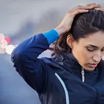 Afbeelding: naar beneden kijkende vrouw met sportkleding aan en handen op het hoofd