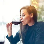 Beautiful young woman drinking red wine with friends in cafe, portrait with wine glass near window. Vocation holidays evening concept