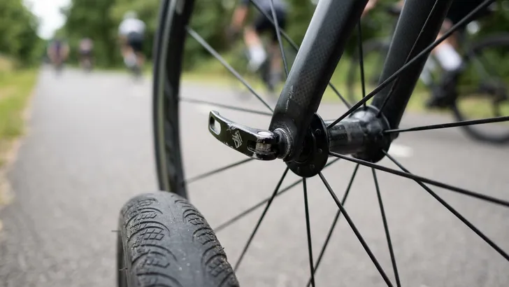 Close-up van een snelspanner op het voorwiel van een racefiets, die gevaarlijk naar voren wijst in plaats van veilig naar achteren.