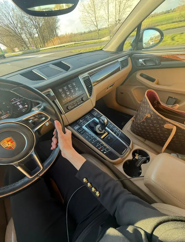 Estelle in de auto met de Louis Vuitton Neverfull naast haar op de stoel. 