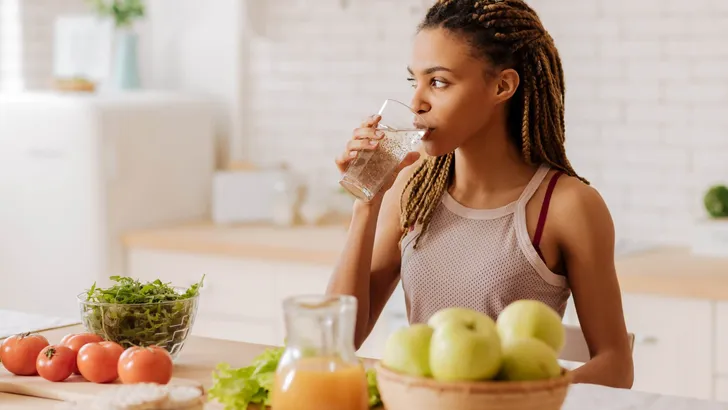 Slim and fit woman drinking water before having breakfast