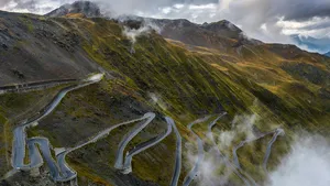Een indrukwekkend herfstlandschap van de iconische Passo dello Stelvio in de Italiaanse Alpen, met een lege, slingerende bergweg zonder gemotoriseerd verkeer.