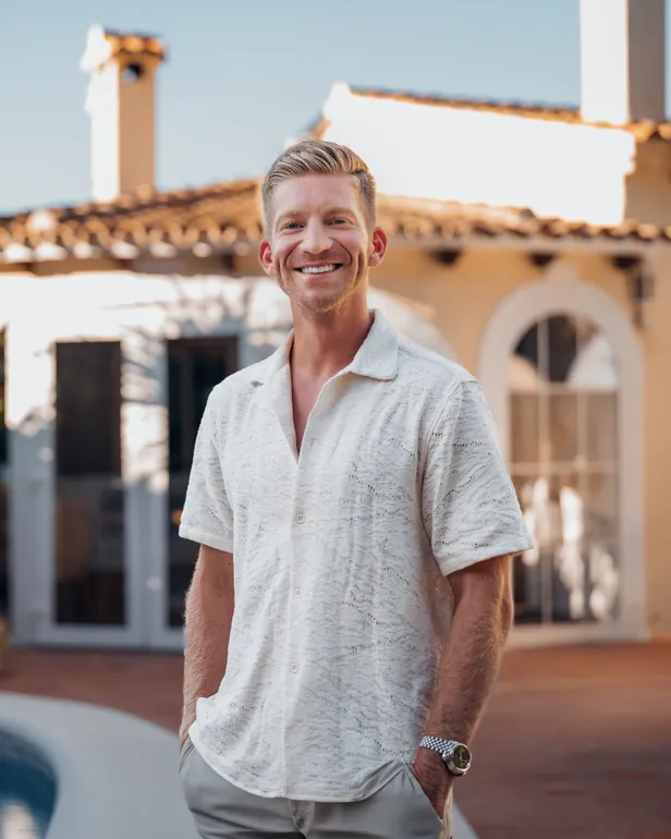 Thomas van B&B Vol Liefde 2026 kijkt lachend in de camera en poseert in een beige polo voor zijn B&B in Dénia, Spanje. 