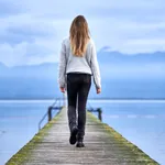 Young blond girl with long hair, standing from the back on a wooden pier