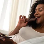 Happy woman enjoying her chocolate bar in bed.