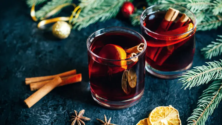 close-up on a hot alcoholic drink mulled wine in two transparent glasses with a cinnamon stick, orange and star anise on a dark  table against the background of Christmas tree branches
