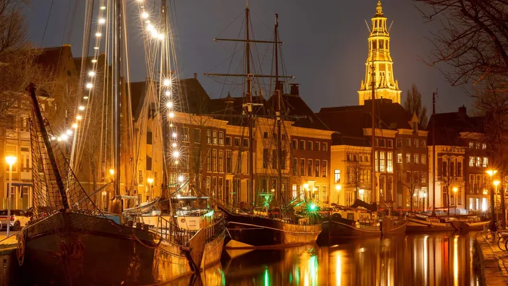 Cityscape of Groningen at night, view of historical ships, canal and tower of the Aa-kerk church