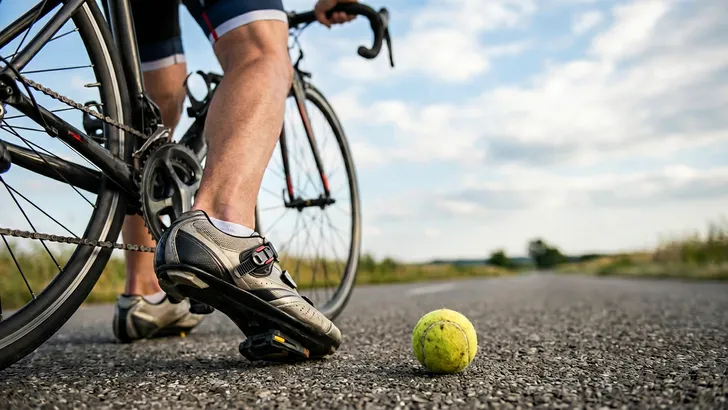 Een mannelijke wielrenner op zijn racefiets en op de voorgrond een tennisbal die symbool staat voor de oplossing van rugpijn bij het fietsen.