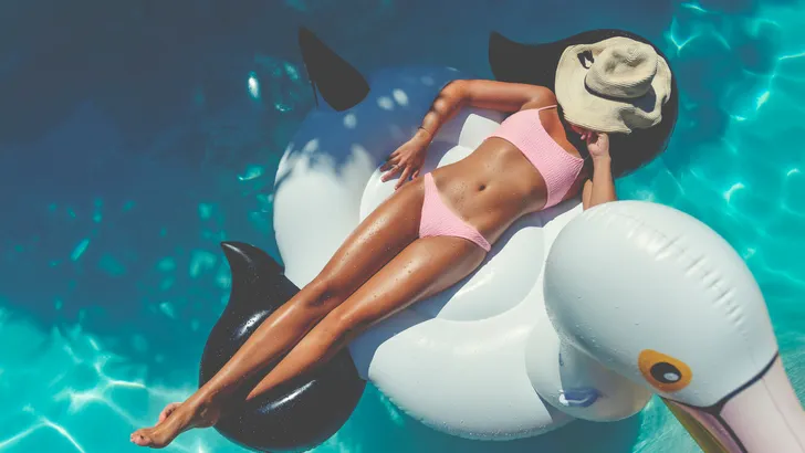 Woman floating on a white inflatable in swimming pool in a pink bikini.