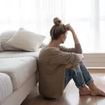 A depressed woman is sitting on the floor in the living room.