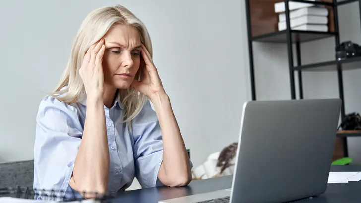 Stressed forgetful old middle aged business woman suffering from headache after computer work. Tired upset 50s lady massaging head feeling stress, fatigue or migraine using laptop at home office.