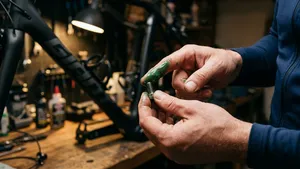Een fietser zonder helm smeert in zijn werkplaats montagevet op de schroefdraad van een klein bidonhouderboutje.