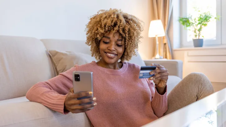 Safe mobile banking. Smiling african lady client hold mobile phone credit bank card do online shopping provide internet payment. Happy young woman enjoy easy fast secure transferring money