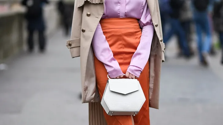 Weekendtips van Beau Monde, week 7 2025 – Foto van stijlvolle vrouw op straat met beige trenchcoat, roze blouse, oranje kokerrok en witte handtas.