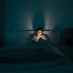 Sleepy woman lying in bed using smartphone late at night, can not sleep. Insomnia, addiction concept