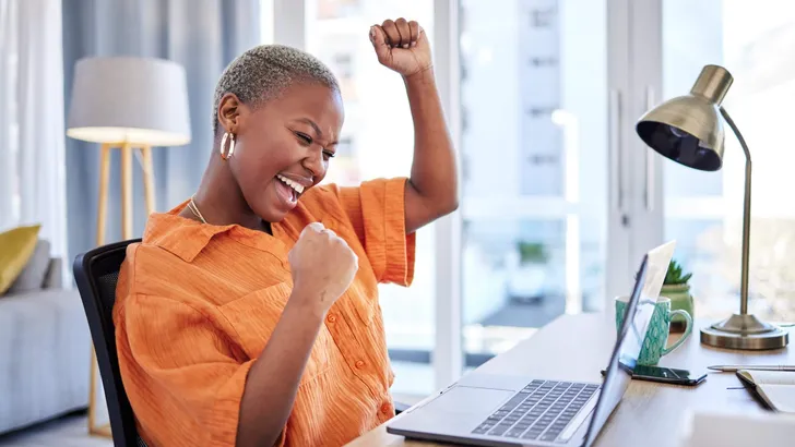 Businesswoman, laptop or winner with fist pump for winning, success or promotion bonus in home office. Happy black woman trader trading or cheering with prize, goal target or good news in remote work
