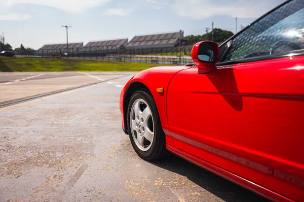 Voorwiel en carrosserie van de rode Honda NSX naast het circuit