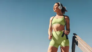 Female athlete in her 30s outdoors taking a break from her cardio workout, holding a skipping rope and wearing sportswear