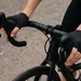 Close-up van een wielrenner met handen op de remgrepen van een racefiets, waarbij stuur en hoods duidelijk zichtbaar zijn voor een stuurstand-check.