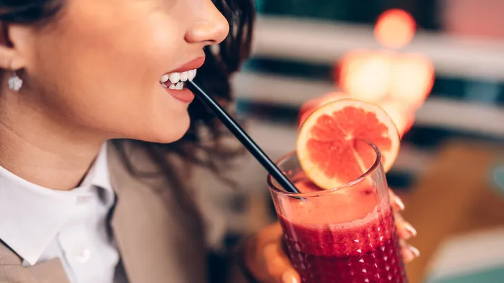 A middle-aged woman  sitting in a cafe and enjoying in a fresh beetroot and grapefruit juice.