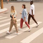 Young happy intercultural friends having drinks and talking while crossing road