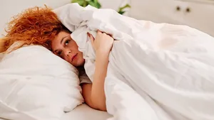 Lazy redhead girl in the bed. A lazy ginger girl lying in her bed in the morning, covering her head with a bed-sheet, and don't want to get up.