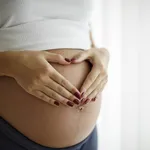 Pregnant woman holding her belly and making a heart shape