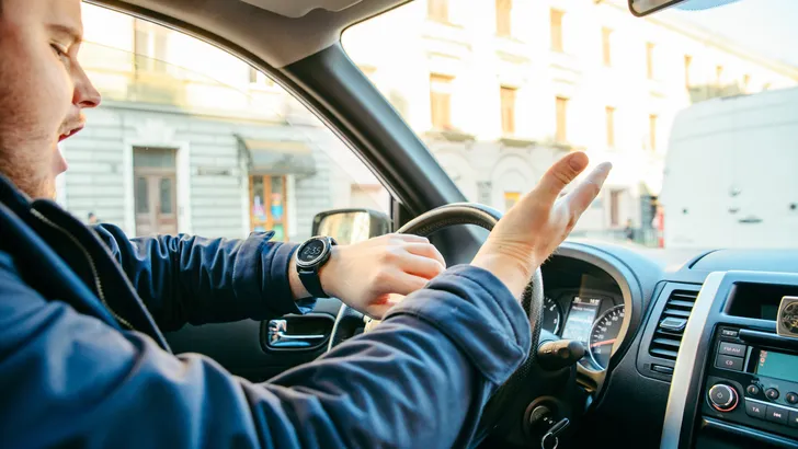 Geïrriteerde automobilist maakt handgebaar achter het stuur in stadsverkeer
