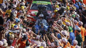 Wielerfans juichen massaal langs de Alpe d’Huez tijdens de Tour de France, terwijl een renner zich een weg baant door de drukte.