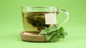 Een glas met een theezakje groene thee tegen een groene achtergrond.