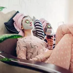 Mother and her adult daughter applied facial masks and cucumbers on eyes. Women chilling while having wine