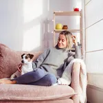 Beautiful middle-aged woman with dog at home sitting on couch