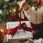 Hands in cozy sweater opening christmas gift with red bow on bac