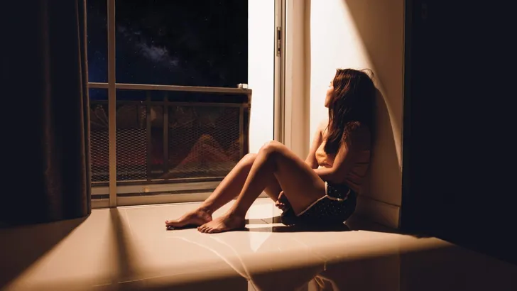 Sad and depressed young woman sitting on the floor in the living room looking outside the doors,sad mood,feel tired, lonely and unhappy concept. Selective focus