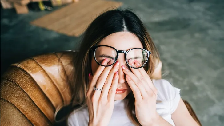 Een vrouw die op de bank ligt en in haar ogen wrijft