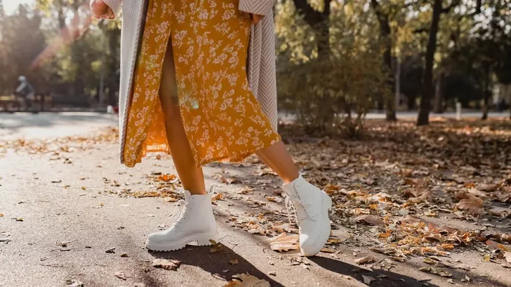 close-up legs in stylish white boots footwear of young woman in yellow printed dress