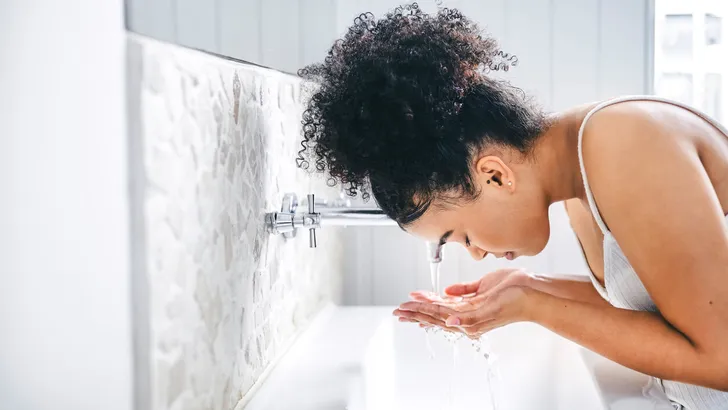 Shot of a young woman washing her face in her bathroom basin