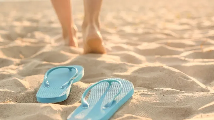 Vrouw loopt op blote voeten naast haar teenslippers.