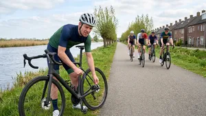 Een gefrustreerde Nederlandse wielrenner zonder helm staat langs een polderweggetje en inspecteert wanhopig de schijfrem van zijn achterwiel als excuus voor slechte benen.