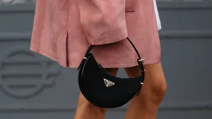Prada koopt Versace voor ruim een miljard euro.  – Streetstyle-foto van vrouw met roze jas en Prada-handtas