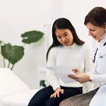 A careful female doctor holding the blood results of a female Asian patient.