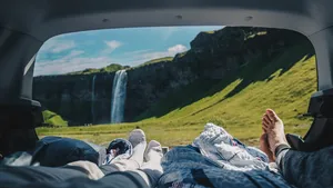 Twee reizigers liggen achterin een auto met uitzicht op een waterval en groen berglandschap