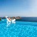 Foto van vrouw op opblaasbed aan rand van infinity pool met uitzicht over zee.