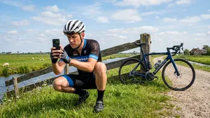 Een ijdele wielrenner hurkt langs de kant van de weg om vol opperste concentratie een foto van zijn geparkeerde racefiets te maken met zijn smartphone.