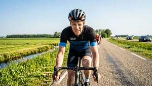 Een wielrenner, vol in actie op een zonnig polderfietspad, wringt zijn gezicht in een pijnlijk wince omdat zweet en zonnebrand in zijn ogen zijn gelopen, als illustratie van een pijnlijke zonnebrandblunder.