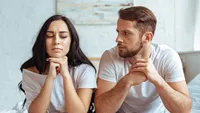 handsome man in jeans and beautiful woman in t-shirt sitting on bed in bedroom