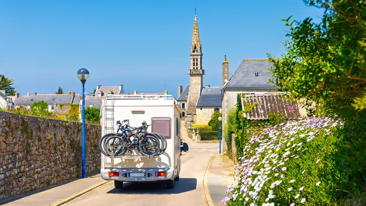 Camper rijdt door een smalle straat richting een traditionele kerktoren in Bretagne, reisbestemming, ontdekkingstocht, roadtrip door Frankrijk