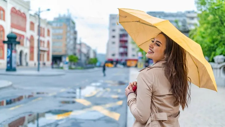 Woman in autumn city. Woman walking on rainy day with yellow umbrella. A portrait of a Long-haired stylish young girl smiling as walking with a umbrella and having fun in the centre of an old city.