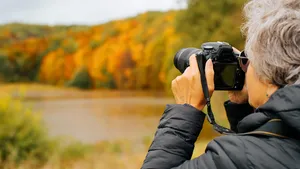 Retirement hobby, seniors and technology concept. Back view senior woman photographer uses digital camera, senior woman takes photo of autumn landscape outdoors, copy space. Selective focus on camera